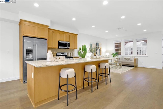 kitchen featuring a breakfast bar area, light stone countertops, an island with sink, and appliances with stainless steel finishes