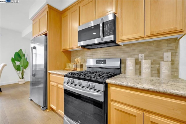 kitchen featuring appliances with stainless steel finishes, light brown cabinetry, light stone counters, and decorative backsplash