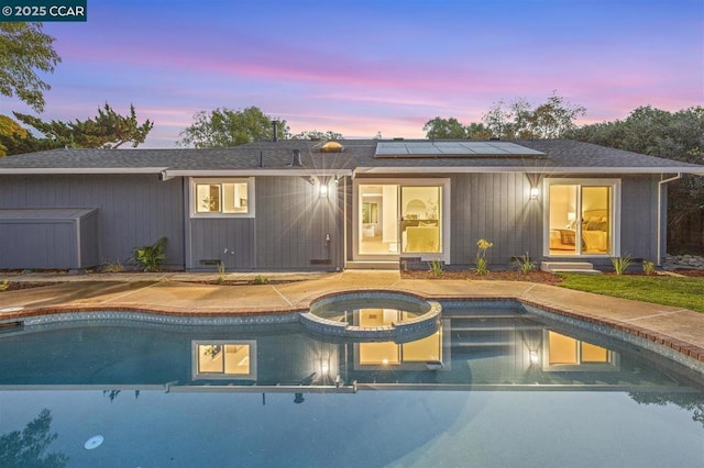 back house at dusk with a pool with hot tub and solar panels