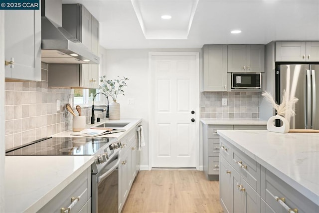 kitchen with gray cabinetry, light stone countertops, wall chimney exhaust hood, and appliances with stainless steel finishes