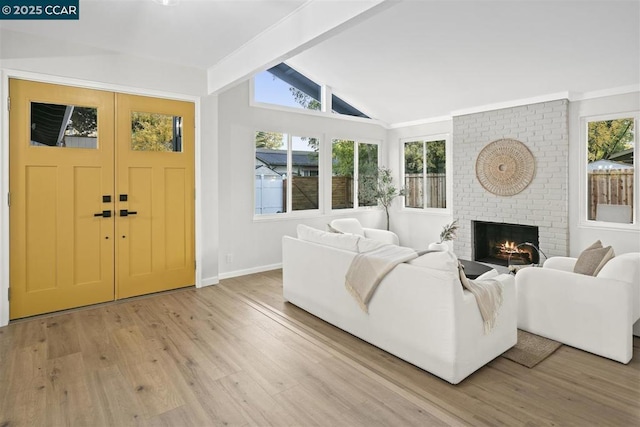 living room featuring a healthy amount of sunlight, a fireplace, lofted ceiling with beams, and light wood-type flooring