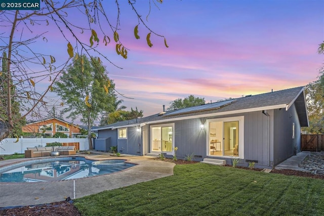 back house at dusk featuring solar panels, a yard, an outdoor living space, a fenced in pool, and a patio