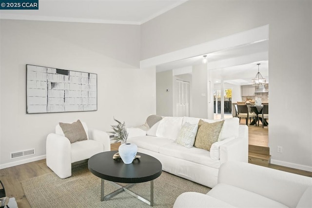 living room featuring wood-type flooring, lofted ceiling, ornamental molding, and a notable chandelier