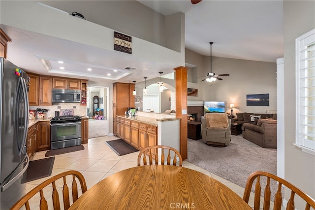 dining area with a brick fireplace, light colored carpet, a raised ceiling, and ceiling fan