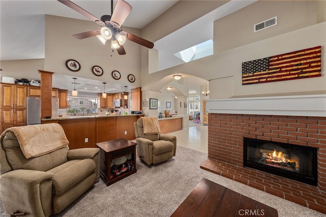 carpeted living room featuring a high ceiling, a brick fireplace, and ceiling fan