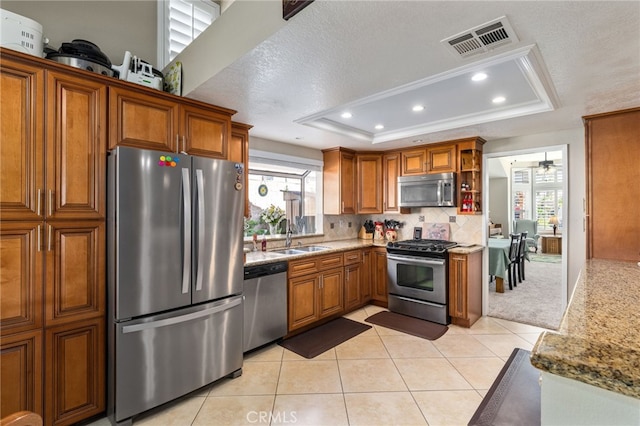 kitchen with light tile patterned flooring, sink, appliances with stainless steel finishes, a tray ceiling, and backsplash