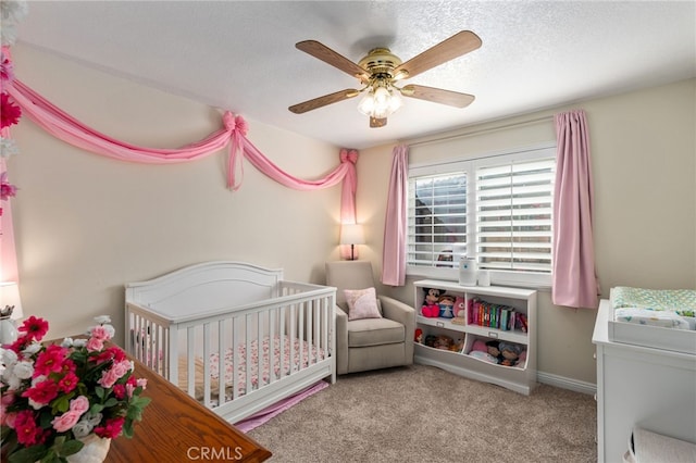 bedroom featuring light carpet, ceiling fan, a crib, and a textured ceiling