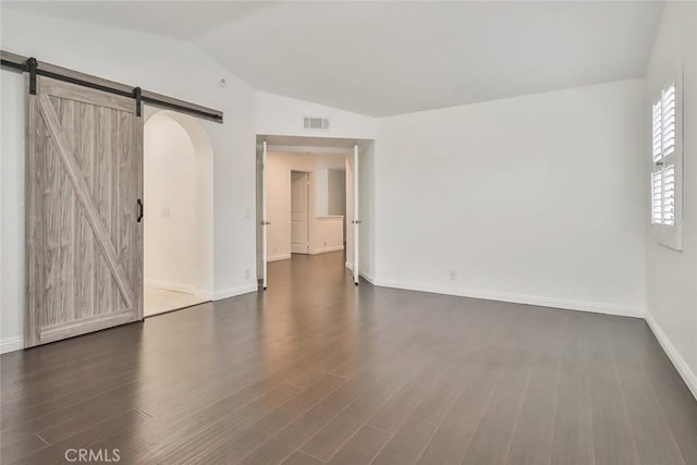 empty room featuring a barn door, lofted ceiling, and dark hardwood / wood-style floors