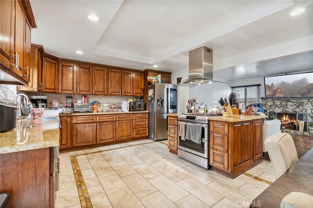 kitchen featuring appliances with stainless steel finishes, island range hood, light stone counters, and decorative backsplash