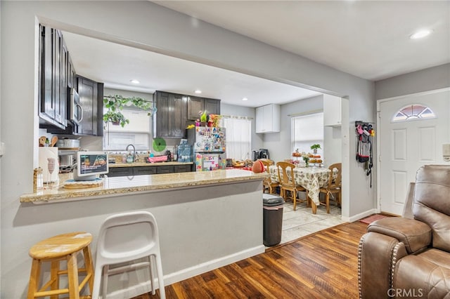 kitchen with a kitchen bar, light stone counters, light hardwood / wood-style flooring, kitchen peninsula, and stainless steel appliances