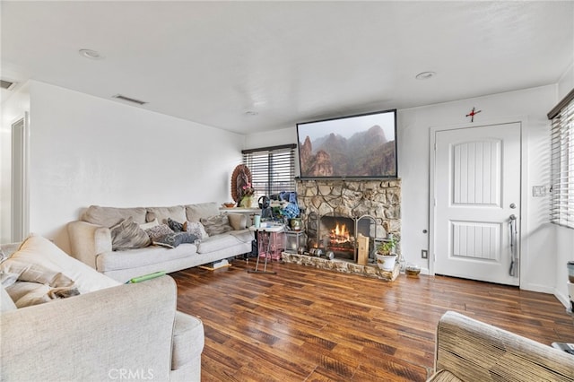 living room with a stone fireplace and dark wood-type flooring