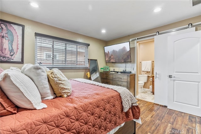 bedroom featuring wood-type flooring, a barn door, and connected bathroom