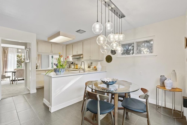 kitchen featuring pendant lighting, sink, dark tile patterned flooring, kitchen peninsula, and cream cabinets