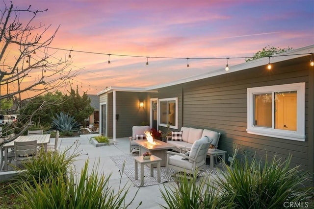 back house at dusk featuring a patio and an outdoor living space with a fire pit