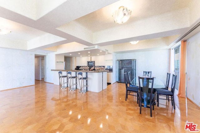 kitchen featuring a raised ceiling, white cabinets, a kitchen bar, and kitchen peninsula