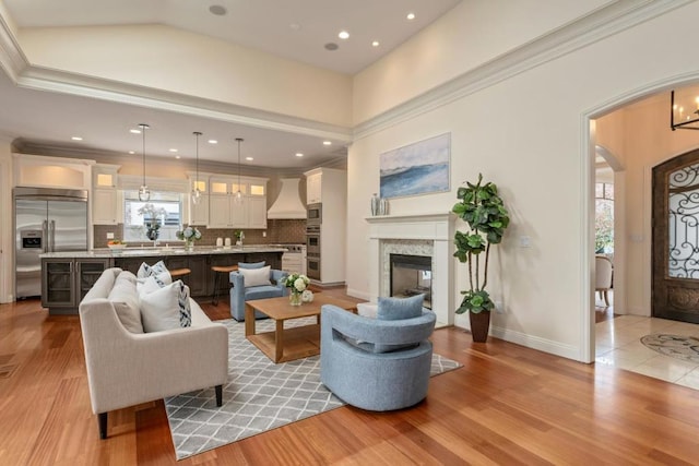 living room featuring a high ceiling, crown molding, a multi sided fireplace, and light hardwood / wood-style flooring