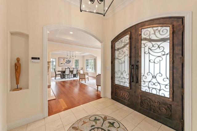 tiled entryway with an inviting chandelier, crown molding, and french doors