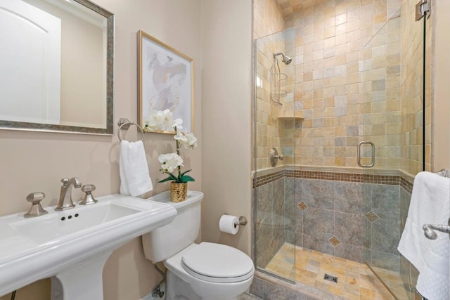 bathroom featuring sink, a shower with shower door, and toilet