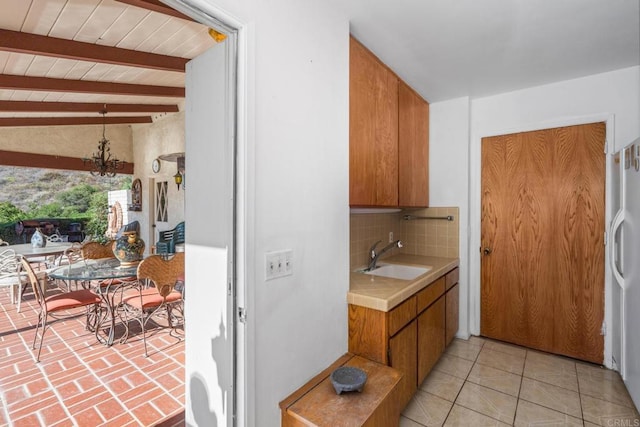 kitchen featuring tasteful backsplash, lofted ceiling with beams, sink, a chandelier, and white fridge