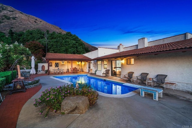 pool at dusk featuring a mountain view and a patio area