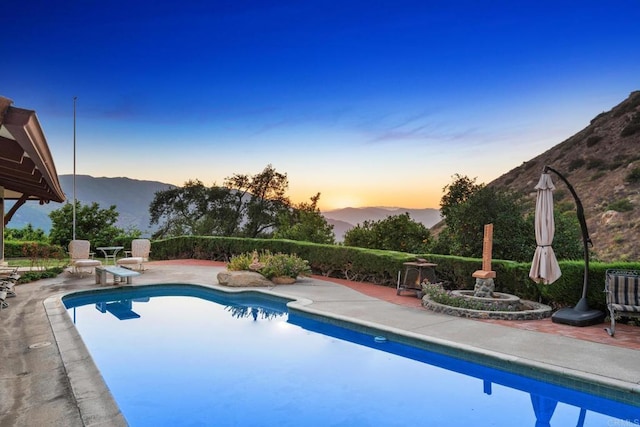 pool at dusk featuring a mountain view and a patio