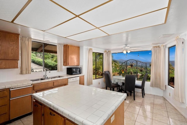 kitchen featuring sink, light tile patterned floors, dishwasher, tile counters, and a kitchen island