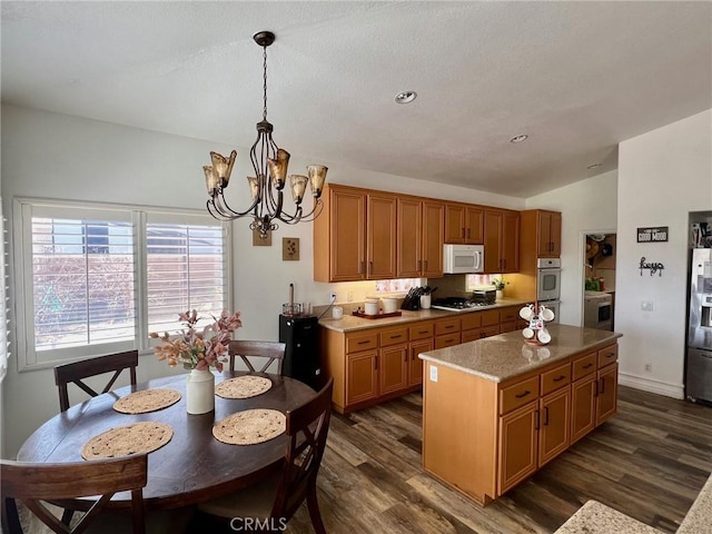 kitchen featuring pendant lighting, lofted ceiling, appliances with stainless steel finishes, a center island, and dark hardwood / wood-style flooring