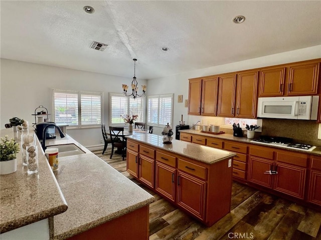 kitchen featuring sink, decorative light fixtures, an island with sink, white appliances, and light stone countertops