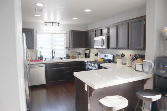 kitchen with a breakfast bar, sink, appliances with stainless steel finishes, dark hardwood / wood-style flooring, and kitchen peninsula