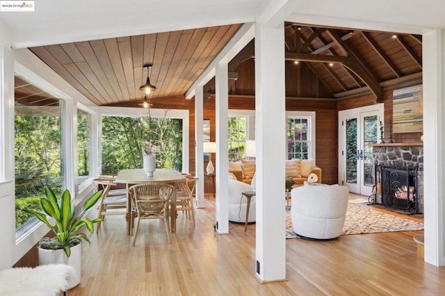 sunroom featuring a healthy amount of sunlight, a fireplace, lofted ceiling with beams, and wooden ceiling