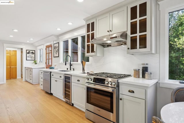 kitchen with sink, light hardwood / wood-style flooring, appliances with stainless steel finishes, decorative backsplash, and beverage cooler