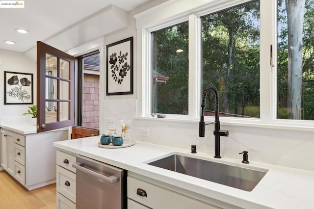 kitchen with sink, white cabinetry, light hardwood / wood-style flooring, stainless steel dishwasher, and decorative backsplash