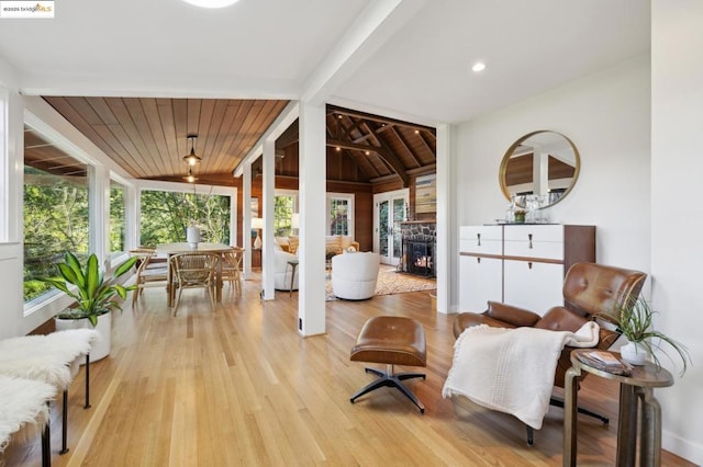 sitting room with lofted ceiling with beams, a stone fireplace, wood ceiling, and light hardwood / wood-style floors