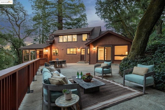 back house at dusk with an outdoor living space, a sunroom, and a patio