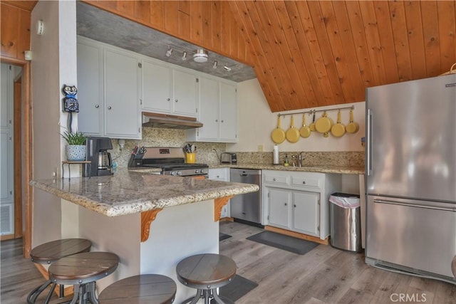 kitchen featuring light stone counters, appliances with stainless steel finishes, kitchen peninsula, white cabinets, and backsplash