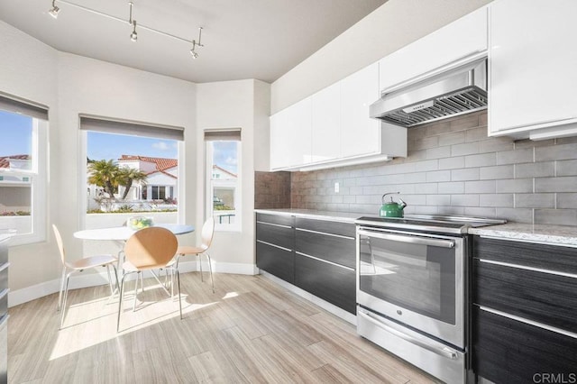 kitchen featuring electric stove, light hardwood / wood-style flooring, white cabinetry, decorative backsplash, and wall chimney exhaust hood