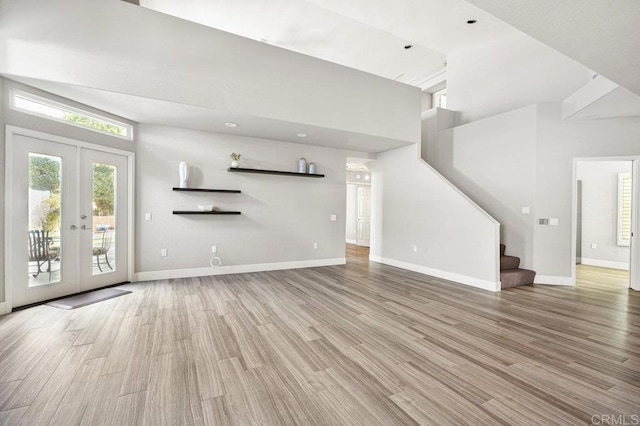 unfurnished living room featuring french doors, a towering ceiling, and light hardwood / wood-style flooring