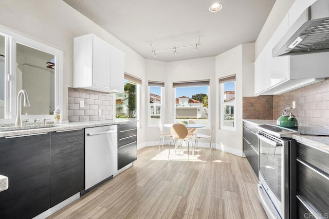 kitchen featuring wall chimney exhaust hood, sink, white cabinetry, light stone counters, and stainless steel appliances