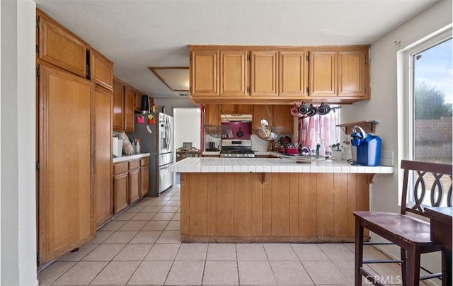 kitchen with appliances with stainless steel finishes, plenty of natural light, tile counters, and kitchen peninsula