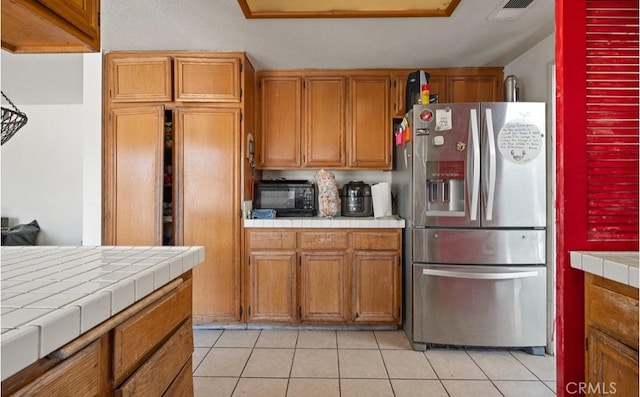 kitchen with tile countertops, stainless steel fridge, and light tile patterned floors