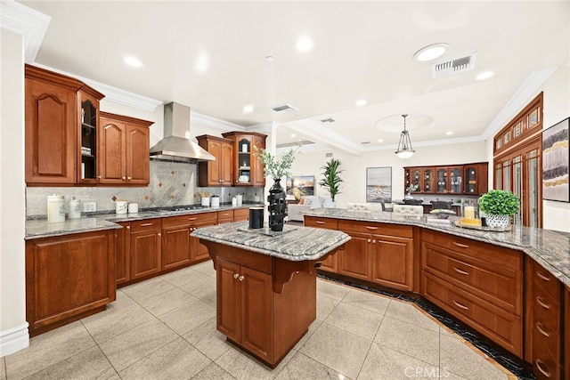 kitchen featuring decorative light fixtures, stainless steel gas cooktop, a center island, light stone counters, and wall chimney range hood