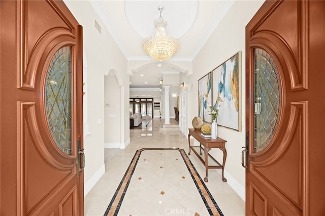 entryway with crown molding, an inviting chandelier, and ornate columns