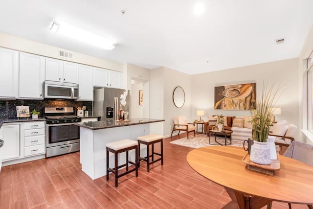 kitchen with white cabinetry, dark stone countertops, stainless steel appliances, light hardwood / wood-style floors, and decorative backsplash