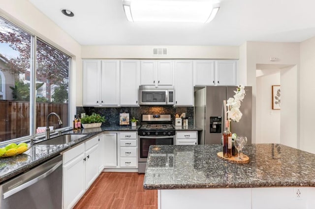 kitchen with appliances with stainless steel finishes, sink, dark stone counters, and white cabinets