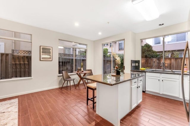 kitchen featuring sink, light hardwood / wood-style flooring, dark stone countertops, white cabinetry, and a center island