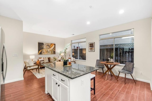 kitchen with a breakfast bar, a center island, light hardwood / wood-style floors, white cabinets, and dark stone counters