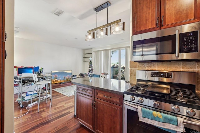 kitchen with appliances with stainless steel finishes, pendant lighting, dark stone countertops, backsplash, and dark wood-type flooring