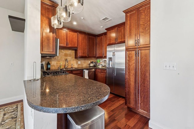 kitchen featuring appliances with stainless steel finishes, pendant lighting, tasteful backsplash, sink, and dark wood-type flooring