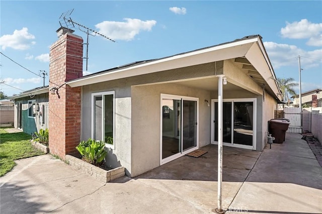 rear view of property with a patio area, a chimney, fence, and stucco siding