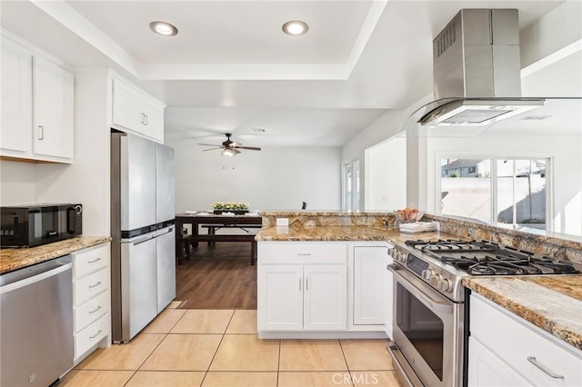 kitchen with appliances with stainless steel finishes, white cabinetry, wall chimney range hood, and light stone counters